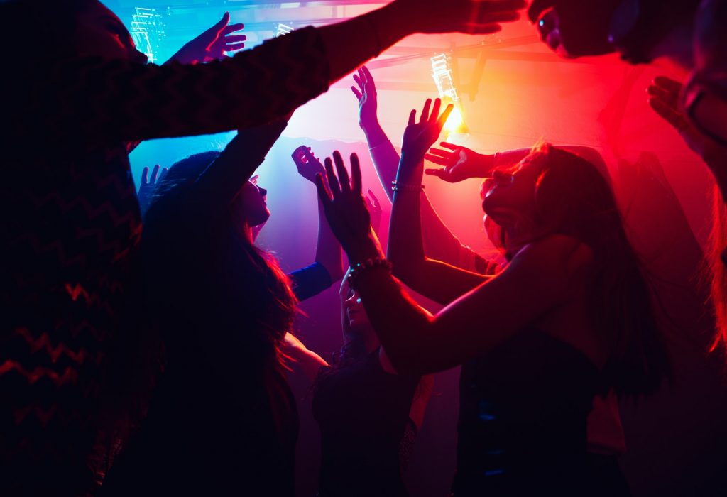 a-crowd-of-people-in-silhouette-raises-their-hands-against-colorful-neon-light-on-party-background.jpg