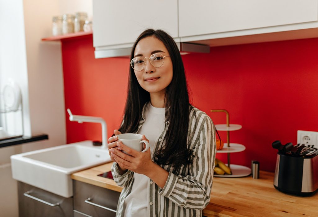 charming-brown-eyed-woman-with-smile-looks-into-camera-and-holds-cup-on-background-of-kitchen.jpg